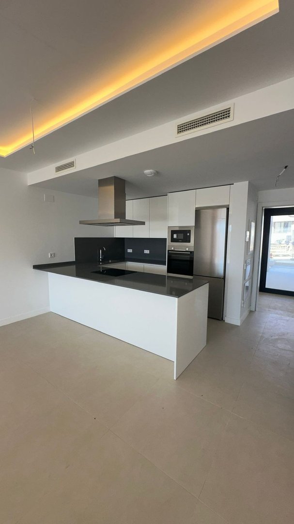Modern white kitchen with a large island, stainless steel appliances, and sleek cabinetry, illuminated by ambient ceiling lighting.