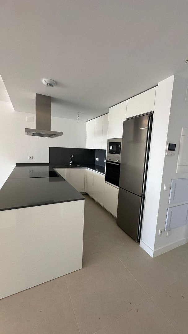 A modern kitchen with white cabinets, a black countertop, stainless steel appliances including a refrigerator, oven, and microwave, and a central island.