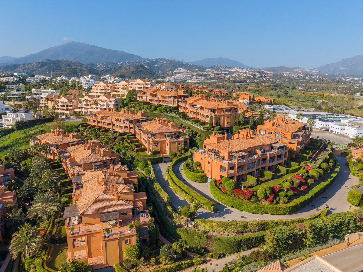 Aerial view of orange apartment buildings on a hillside with manicured gardens and distant mountains.