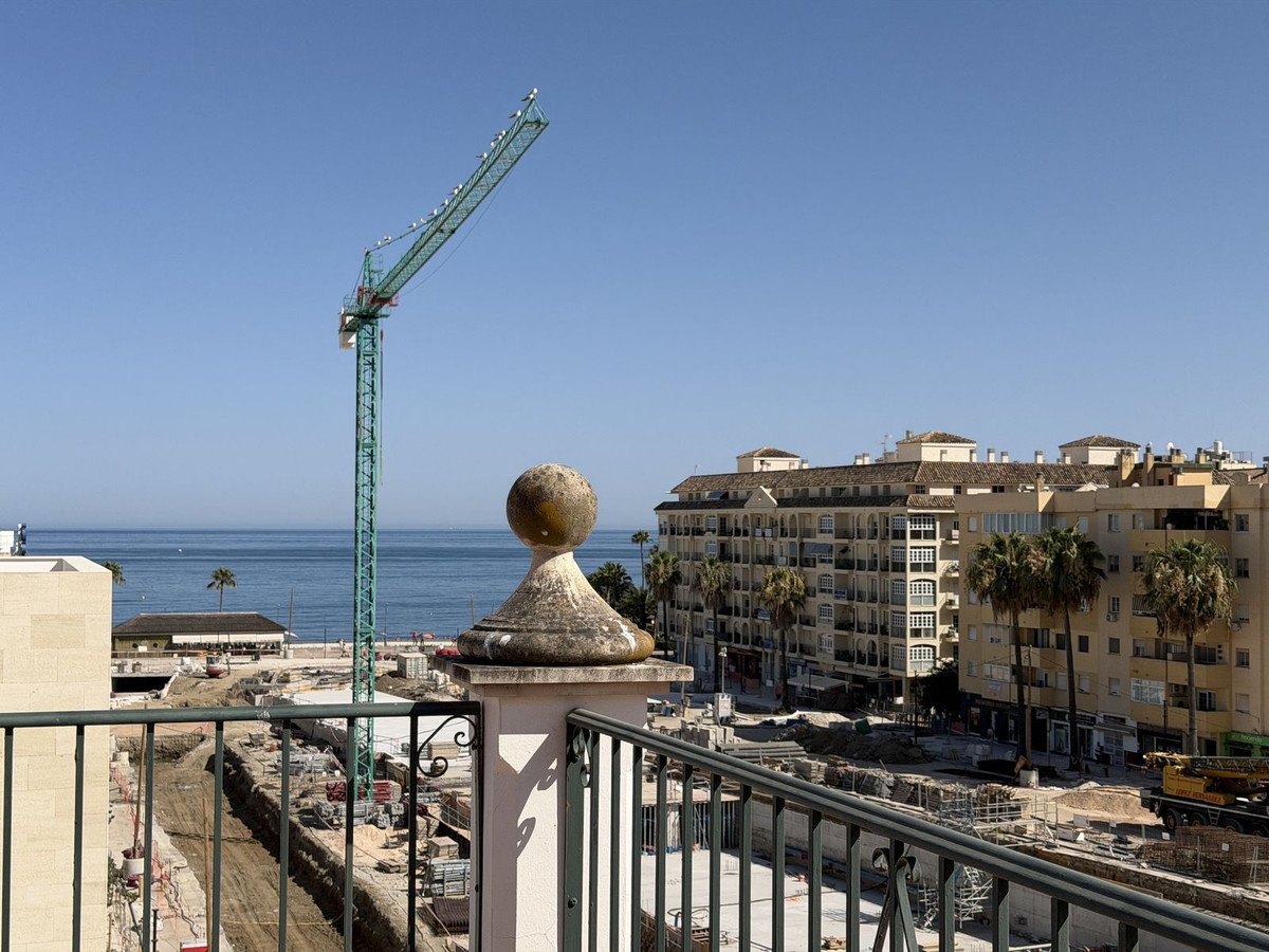 View of the sea and buildings with a construction crane and ongoing development from a balcony railing.