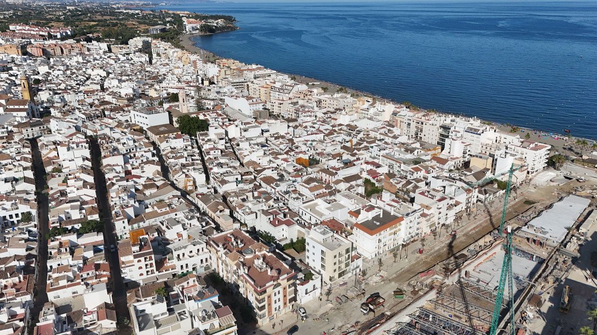 Aerial view of a coastal town with white buildings, a beach, and the blue sea under a clear sky.