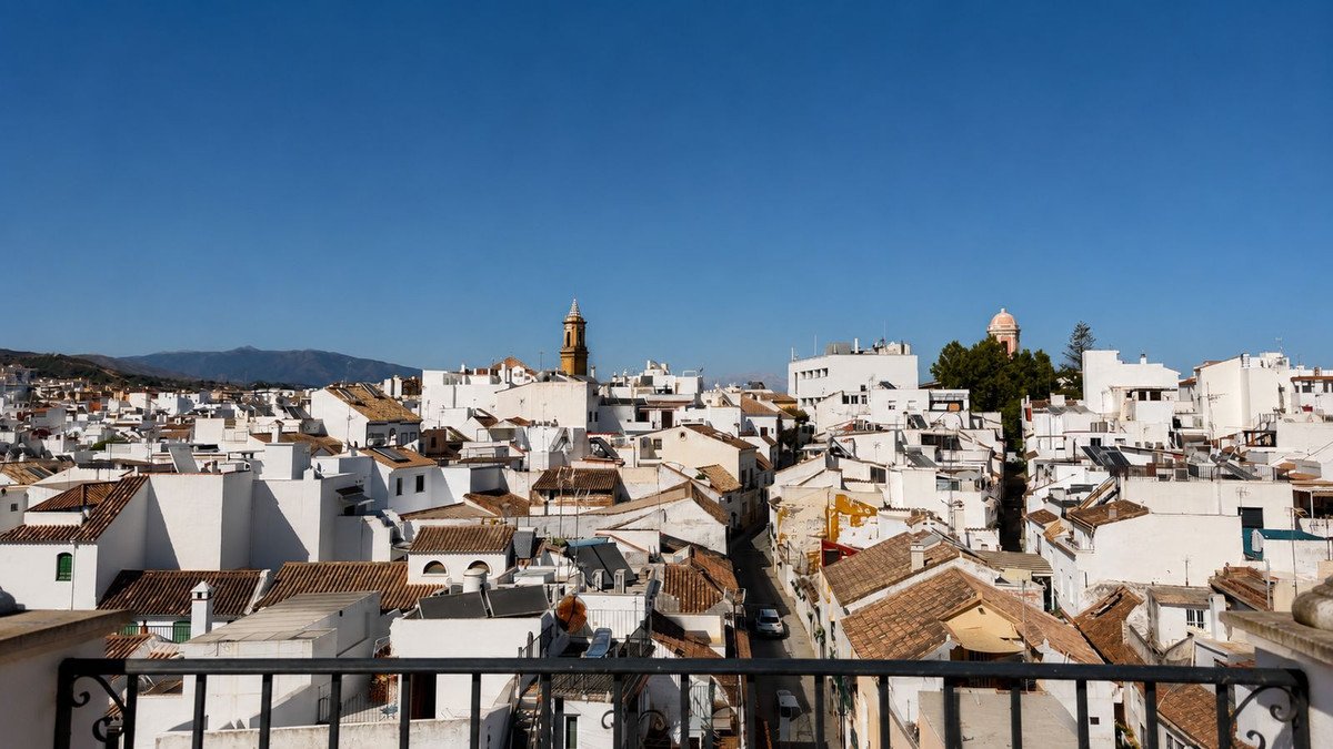 Panoramic view of a white village with tiled roofs and mountains in the distance under a clear blue sky.
