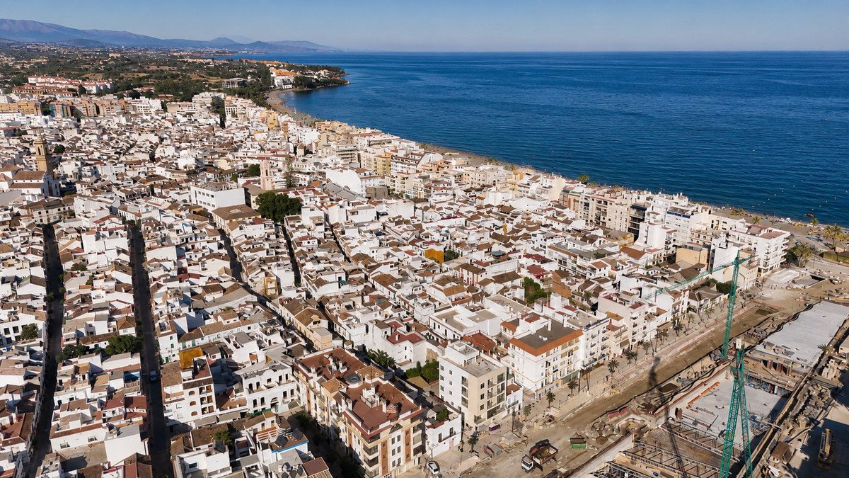 Aerial view of a coastal town with white buildings, a beach, and the blue sea under a clear sky.