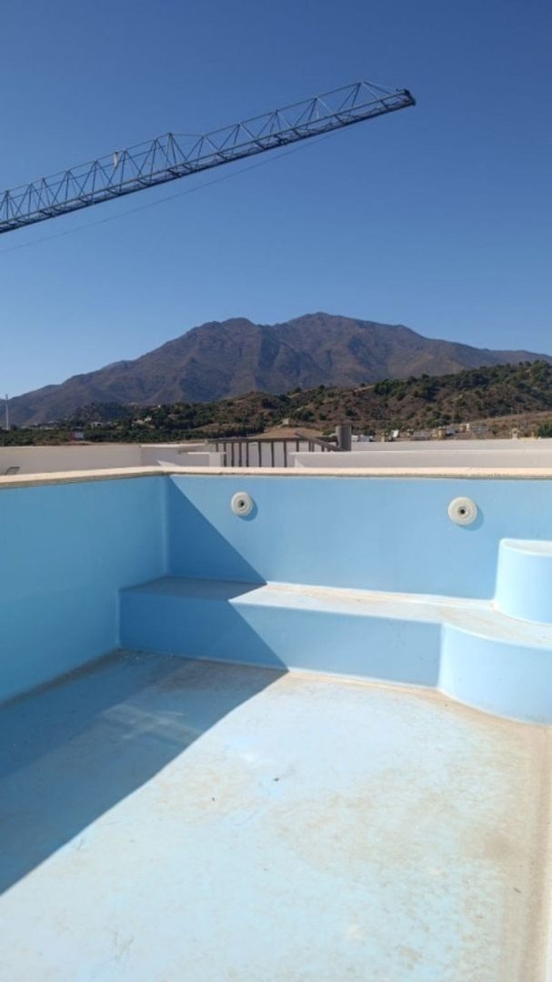 Empty swimming pool with built-in steps, overlooking a mountain landscape under a clear blue sky.
