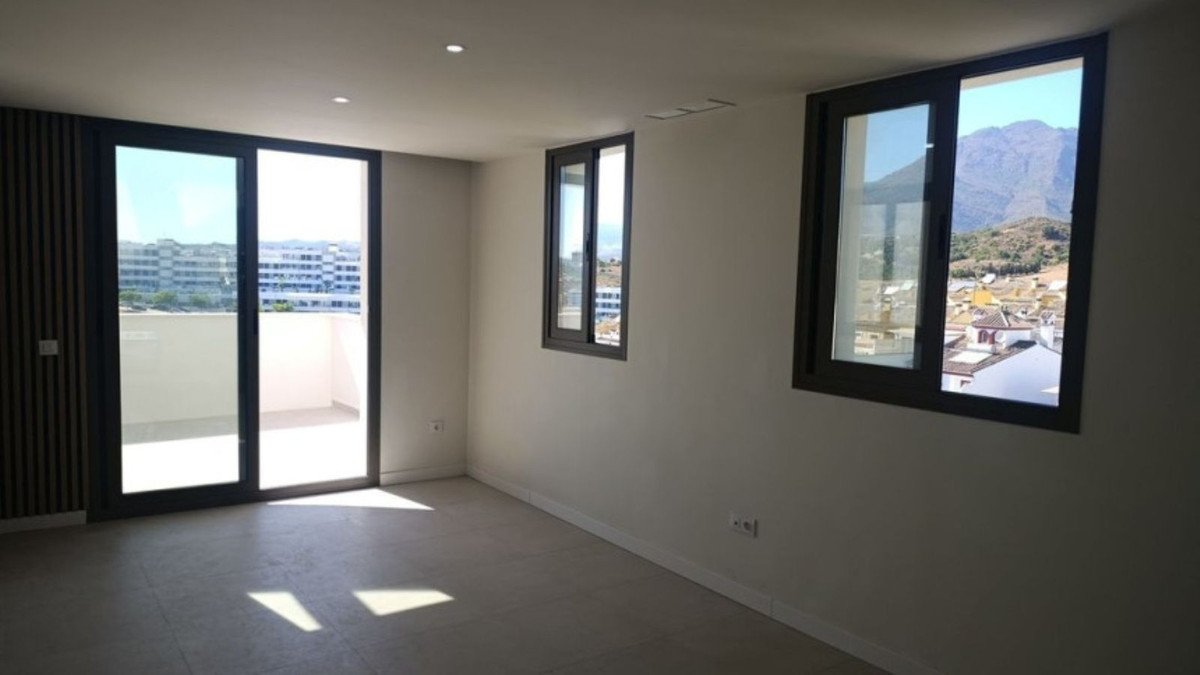 Modern living room with large sliding doors opening to a balcony and windows offering mountain and town views.
