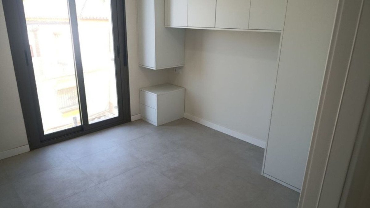 A modern bedroom with built-in storage cabinets, a large window with an external view, and grey tiled flooring.