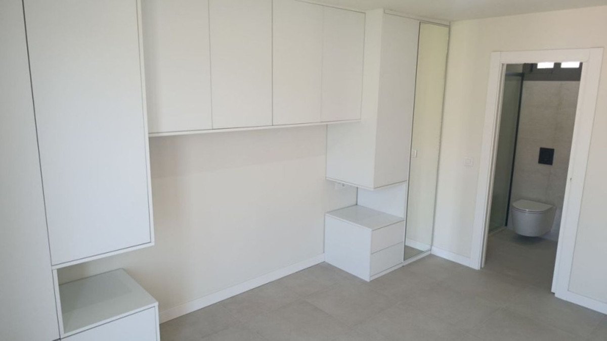 A modern bedroom with abundant built-in white storage cabinets and a doorway leading to a bathroom with a toilet and shower.