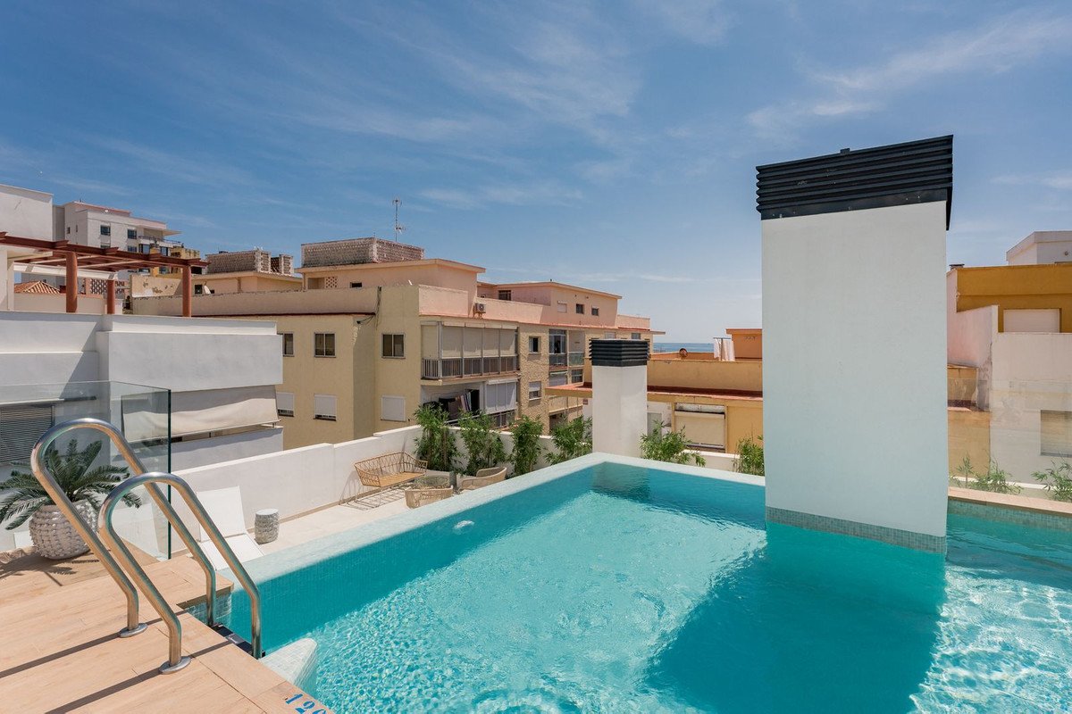 Modern rooftop pool with town views and ocean in the distance. Includes lounge area and sunbeds.
