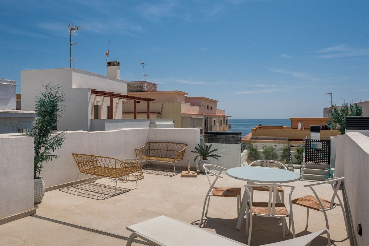 Spacious rooftop terrace with lounge seating, dining table, chairs, and a distant view of the sea.