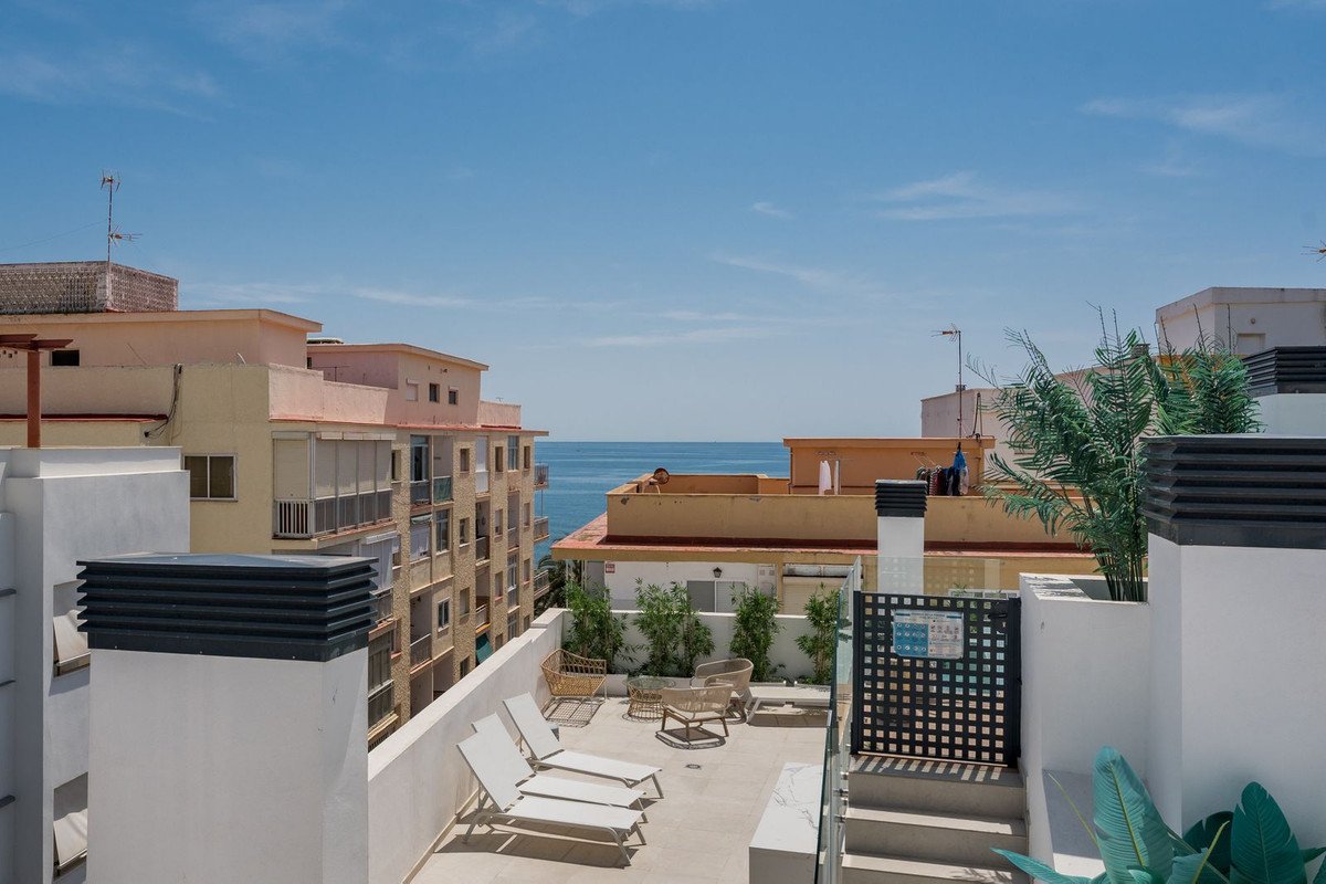 A bright rooftop terrace with lounge chairs, seating area, and a beautiful sea view under a clear blue sky.