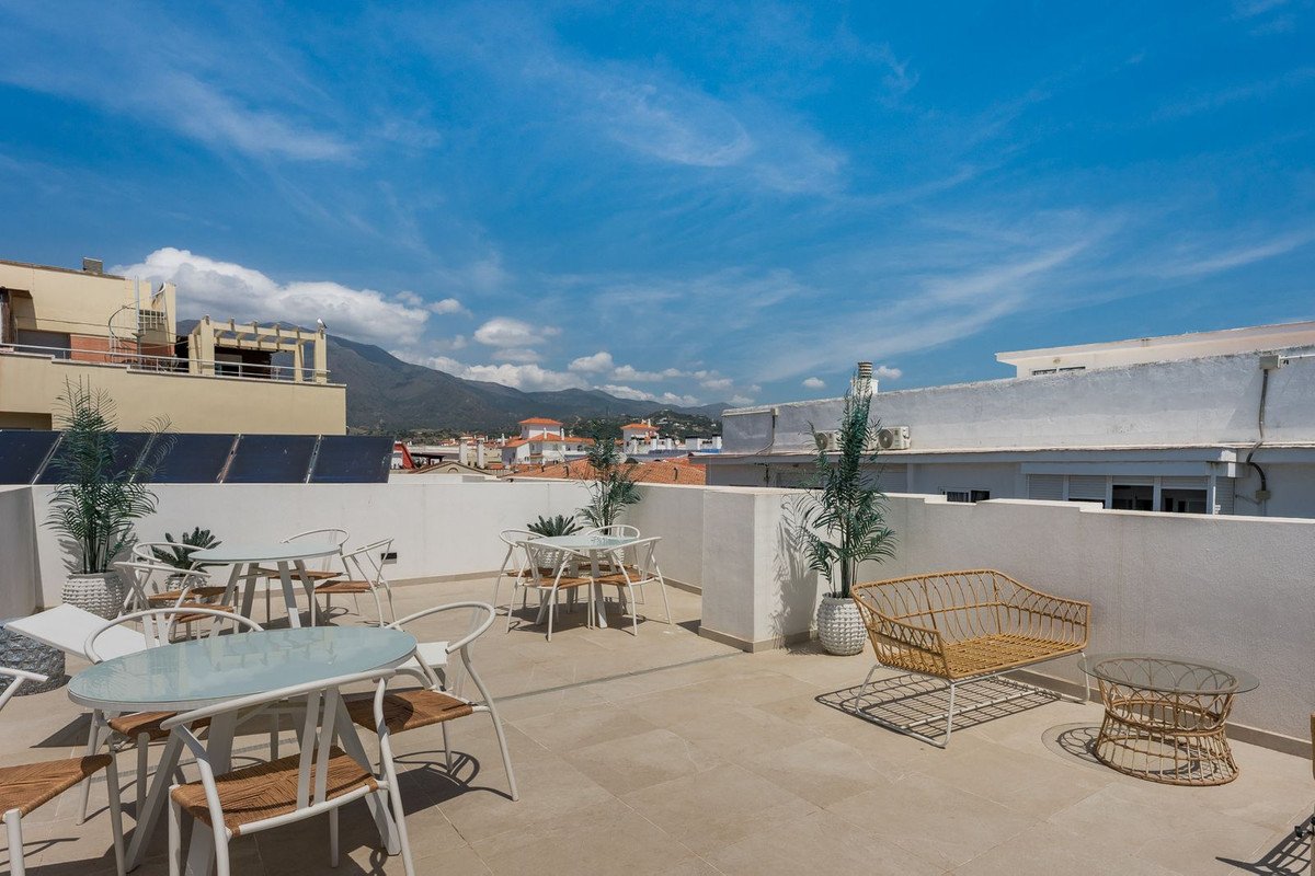 A spacious terrace with outdoor seating and tables, offering a view of mountains under a clear blue sky.