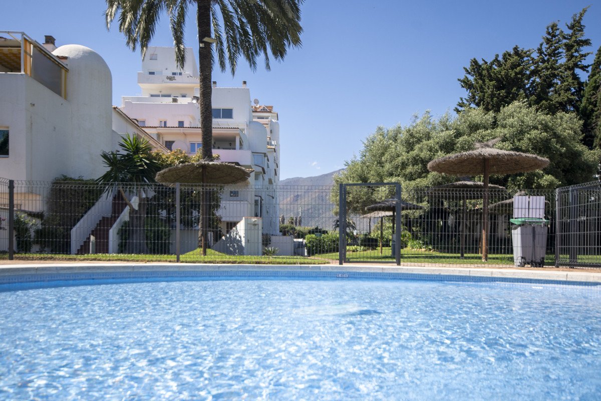 Swimming pool with tropical umbrellas and white buildings in the background