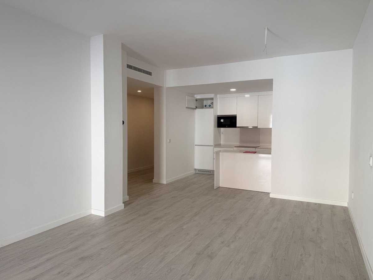 Modern kitchen with white cabinets, microwave, and light wood flooring in an open-plan space.