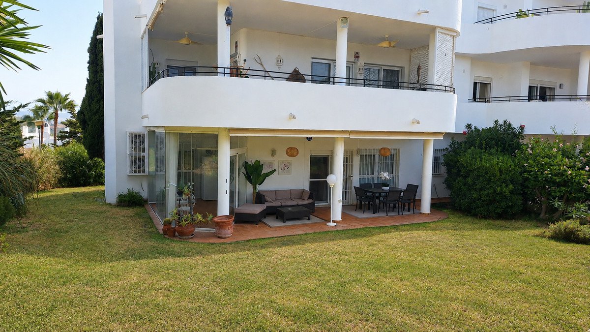 Ground floor terrace with outdoor seating and dining area, overlooking a green garden and palm trees.