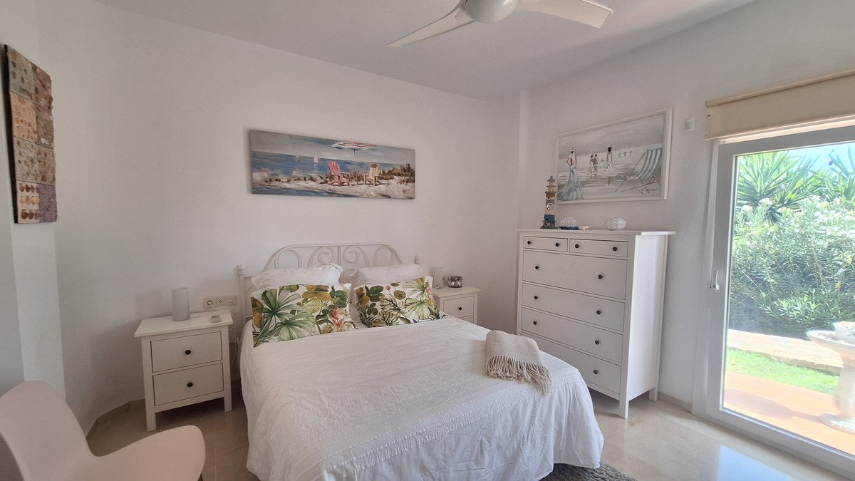 A bedroom with a king-size bed, bedside tables, dresser, and a door leading to a lush green garden.