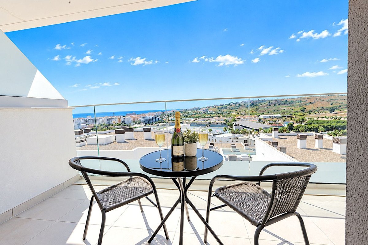 A balcony with two chairs, a table with champagne and glasses, overlooking a town and the sea.
