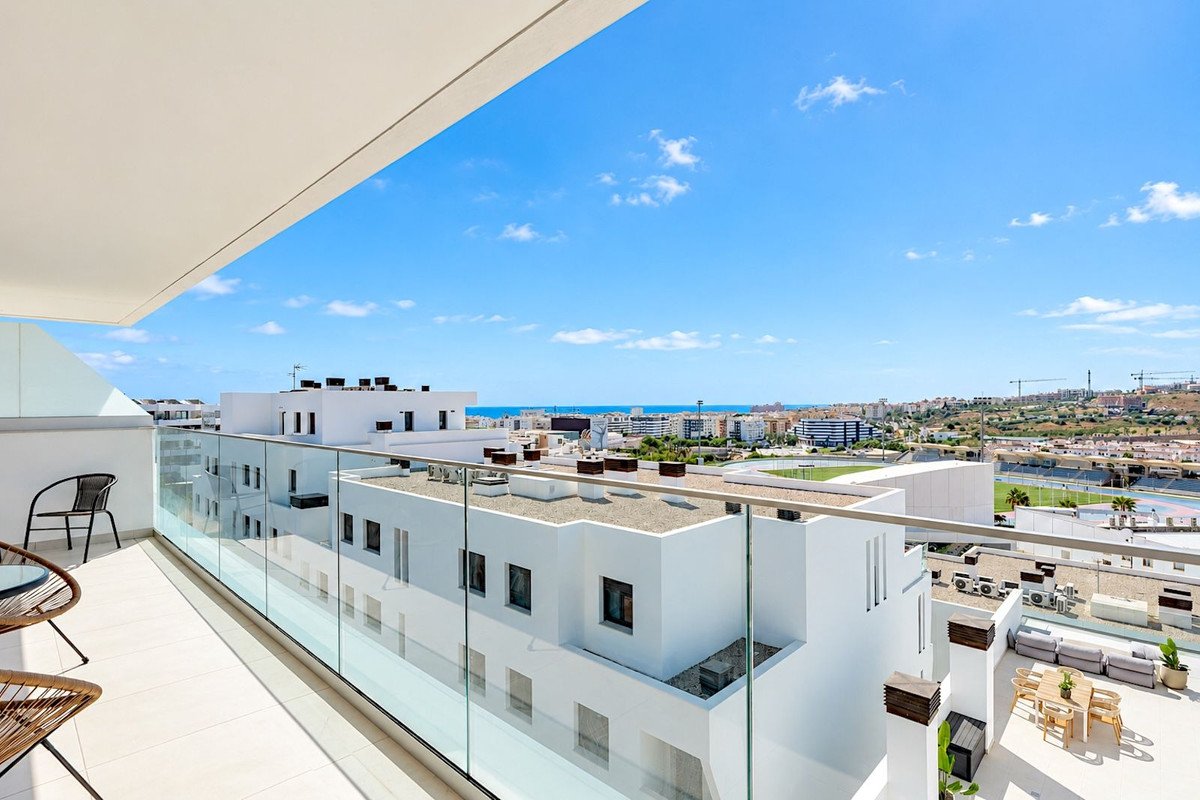 Modern balcony with glass railing, offering expansive sea and city views under a clear blue sky.