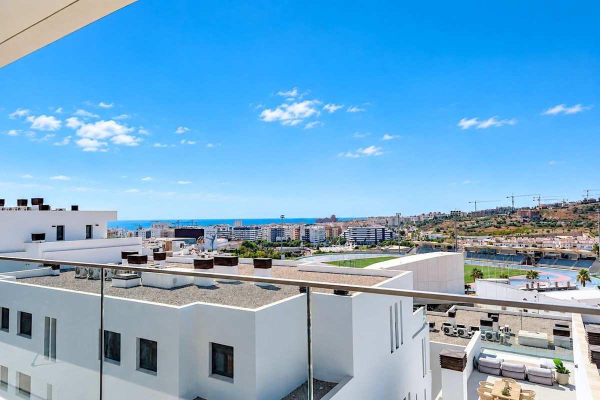 Balcony view overlooking a city and the sea, with modern buildings and a stadium in the distance.