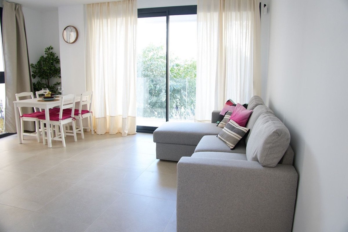 Spacious living and dining area with large windows offering a garden view and a comfortable grey sectional sofa.
