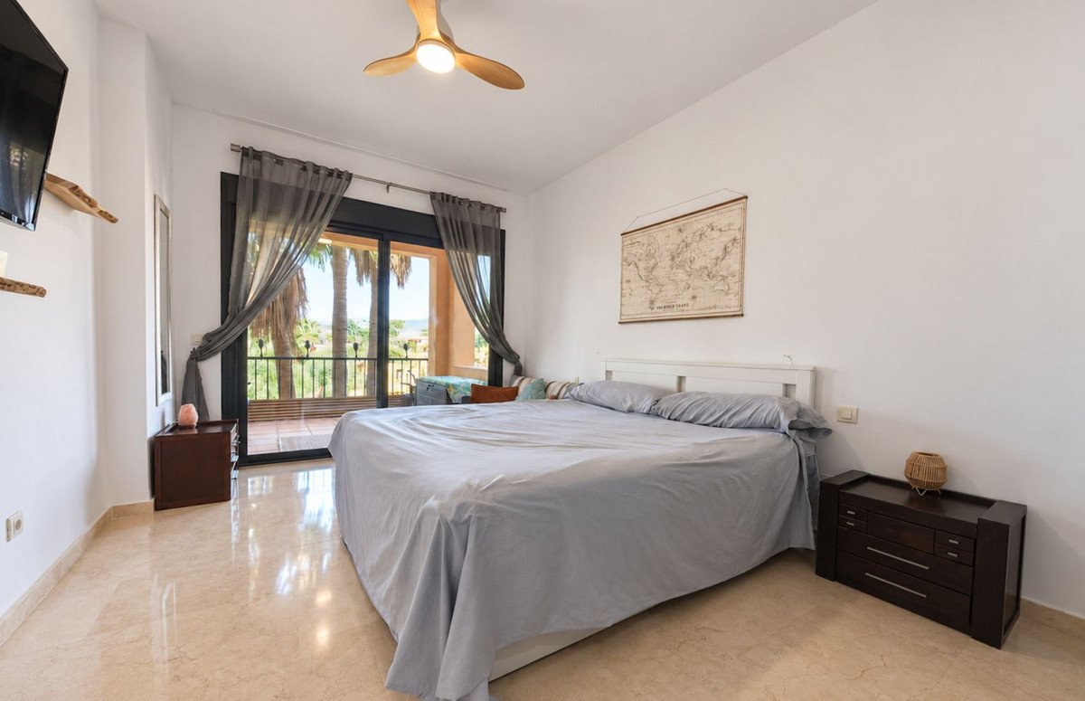 A spacious bedroom with a large bed, ceiling fan, and a balcony with a sea view overlooking palm trees.