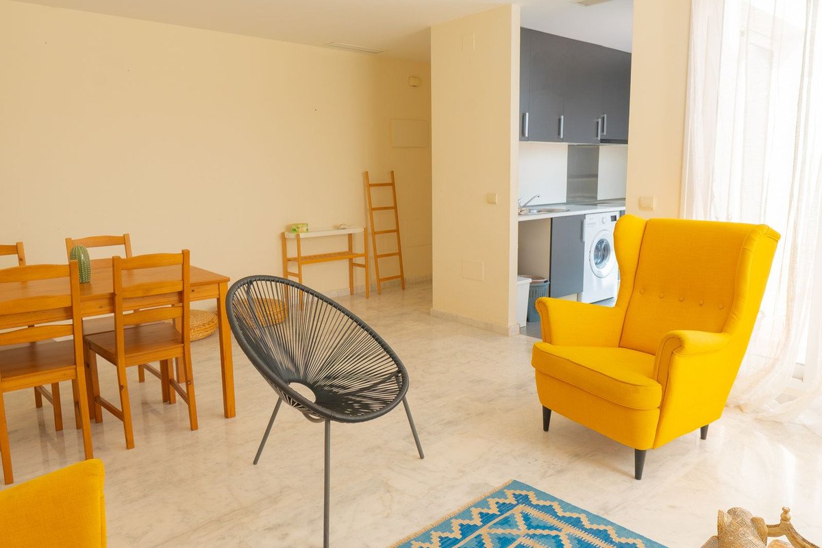 Bright living and dining area with a yellow armchair, a round black chair, and a wooden dining table with chairs.