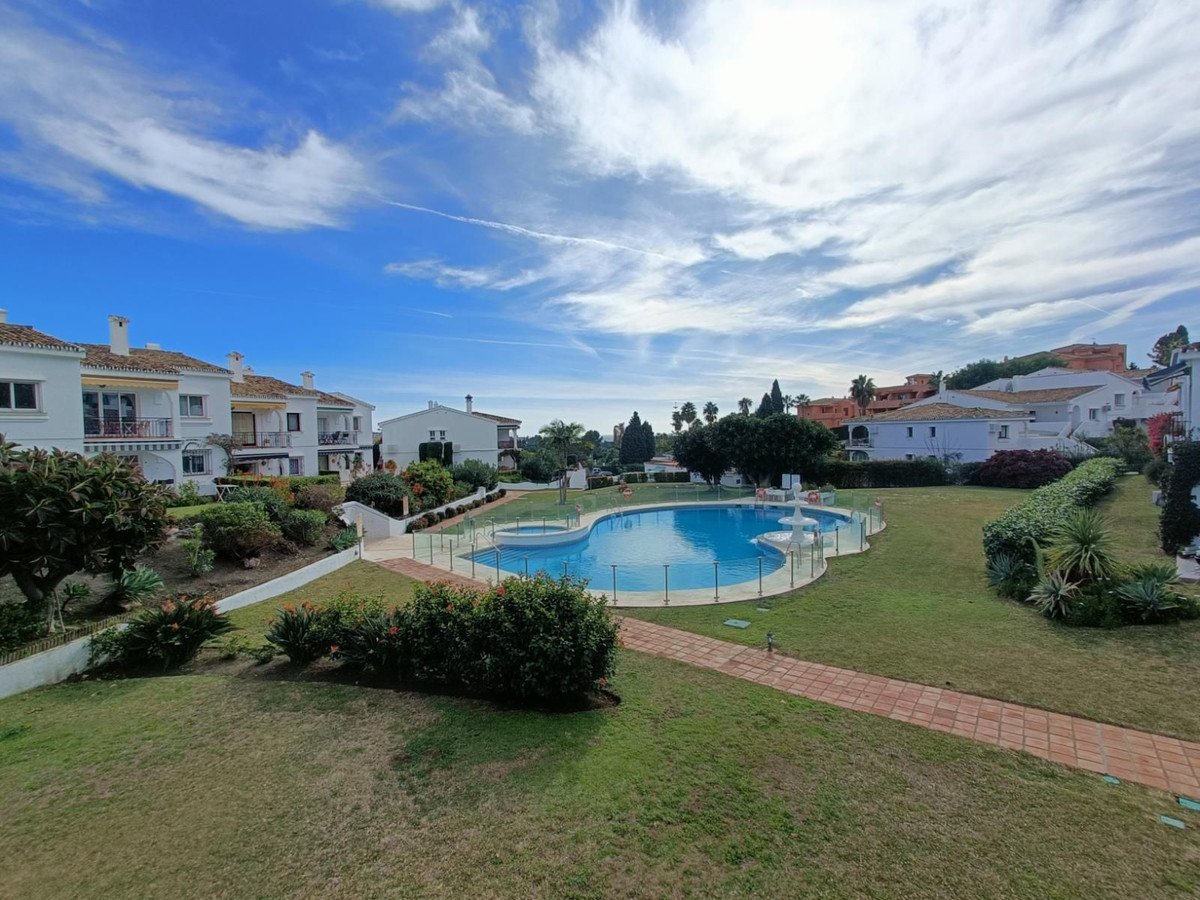 Exterior view of apartments with a swimming pool and green lawn under a cloudy blue sky.