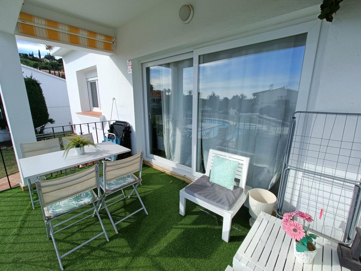 A balcony with a table and chairs overlooking a swimming pool, featuring artificial grass and outdoor seating.