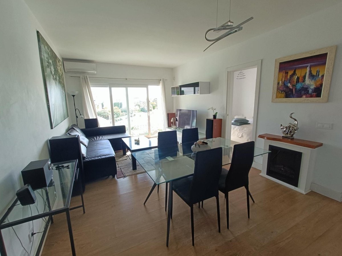 A modern living and dining room with a black sectional sofa, glass dining table, and large sliding doors offering a view of greenery.