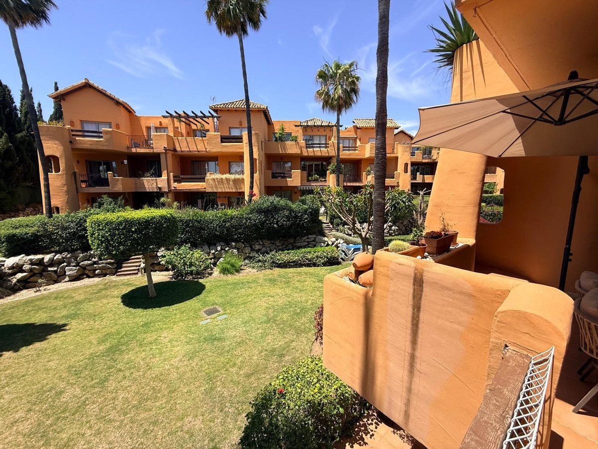 Terrace view of a sunny resort with orange buildings, palm trees, and a green lawn.