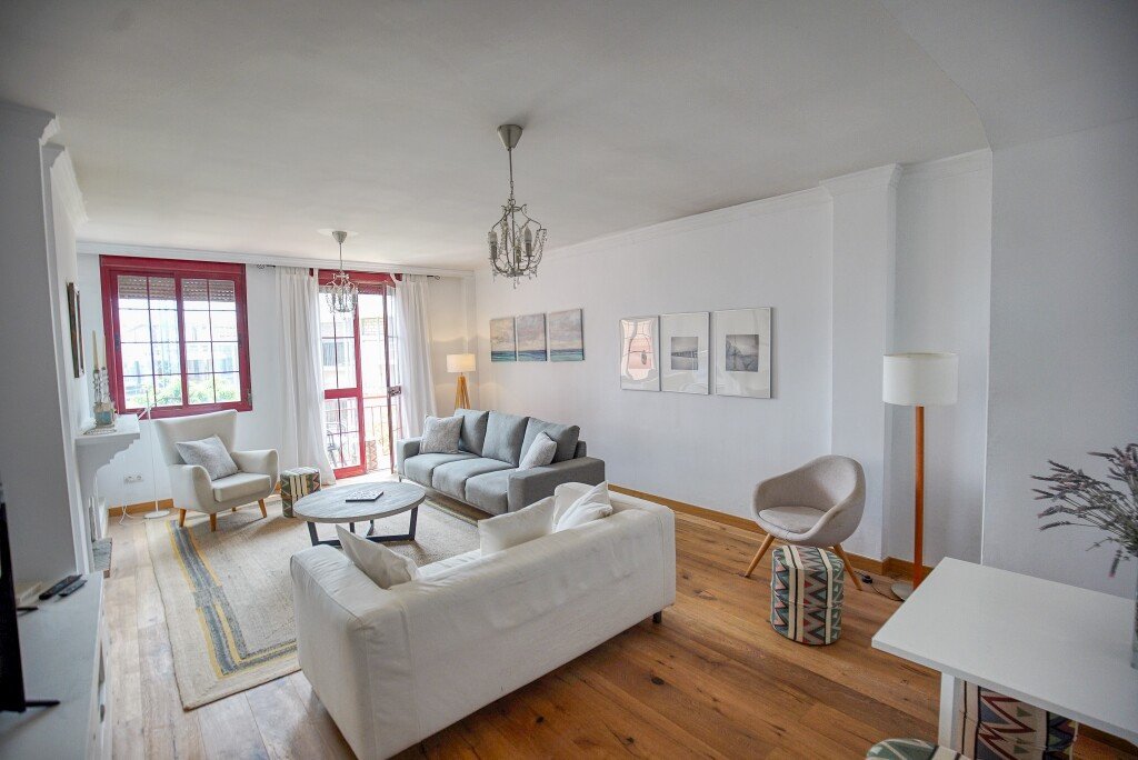 Modern living room with white sofas, red-framed windows, and minimalist decor