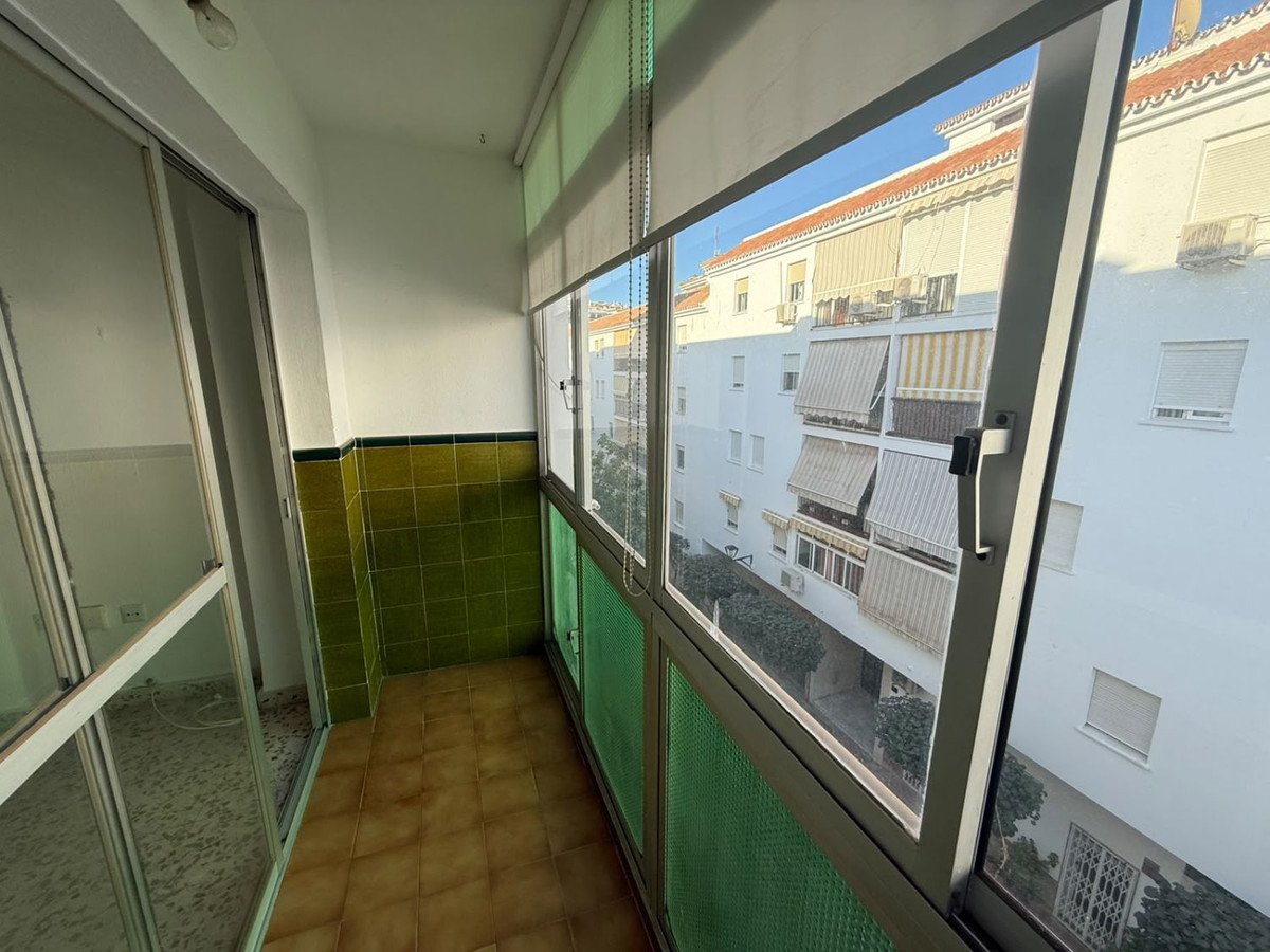 Enclosed balcony with tiled walls and floor, offering a view of apartment buildings with awnings.