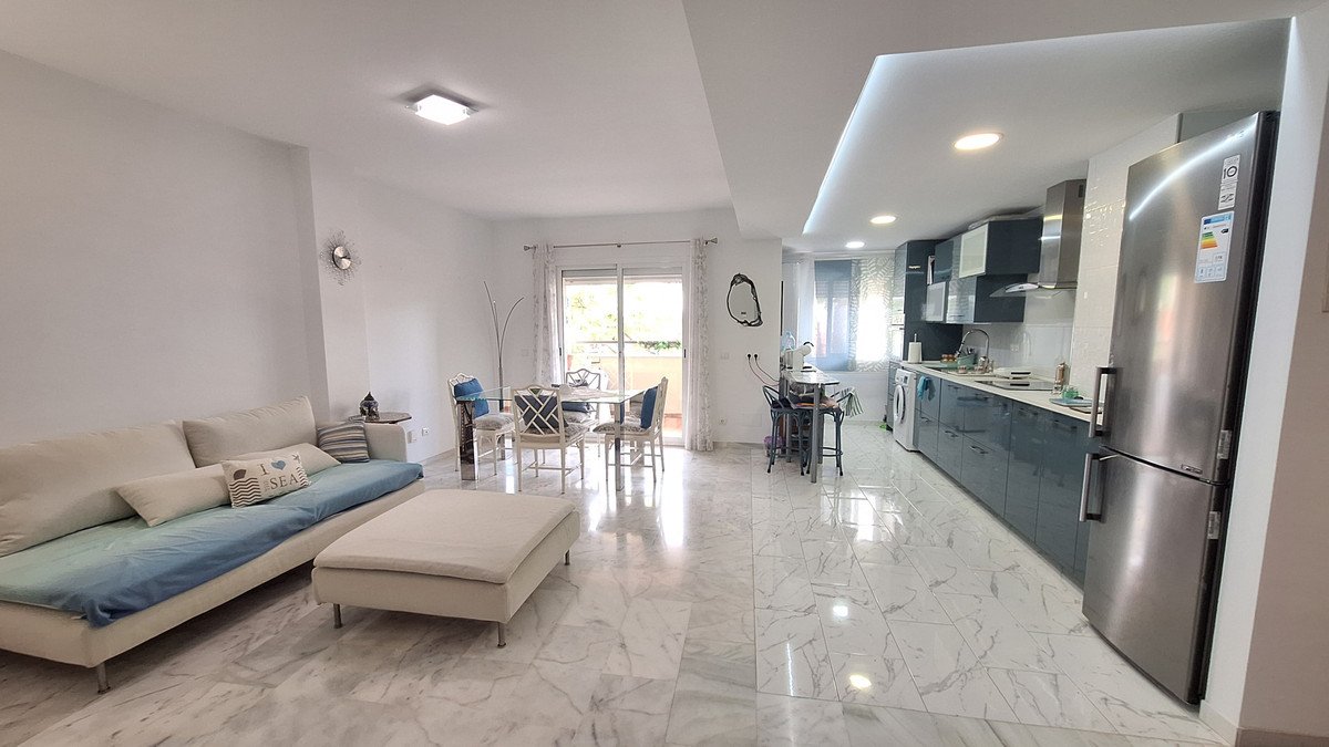 Modern living room with kitchen and dining area, featuring a beige sofa, marble flooring, and large windows with a view