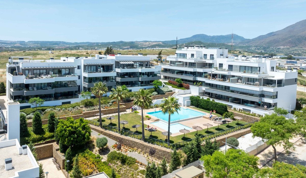 Modern white apartment complex with pool, palm trees, and mountain views.