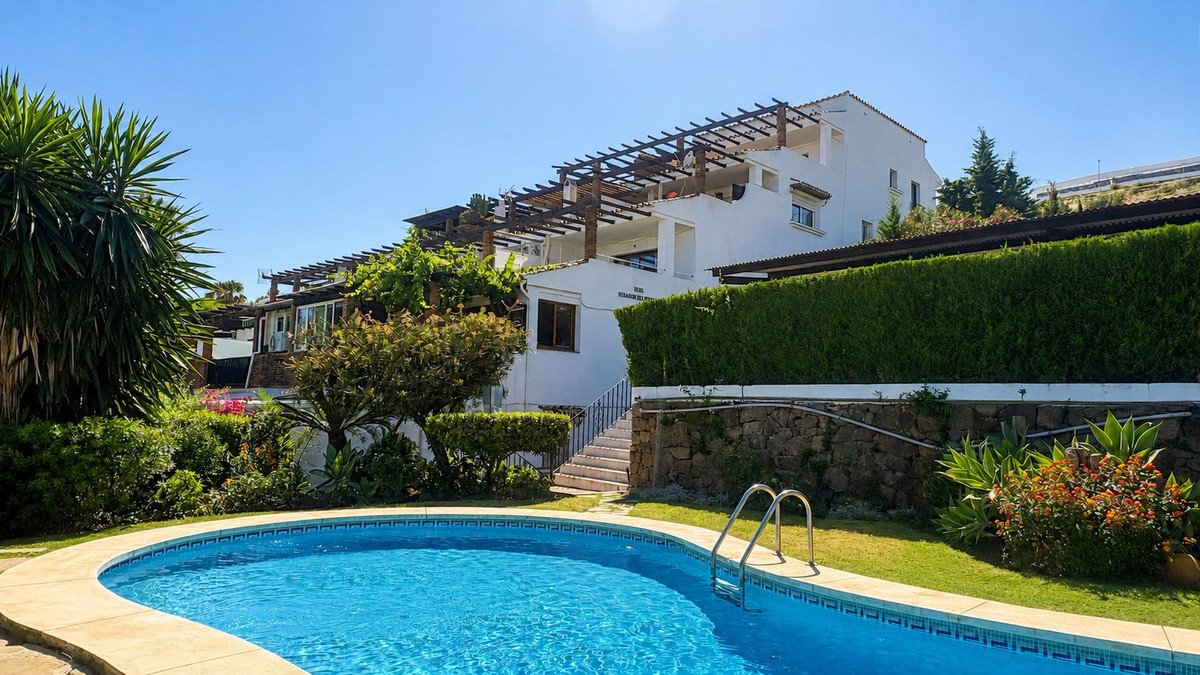 Villa with private pool, lush greenery, and white exterior under clear blue sky.