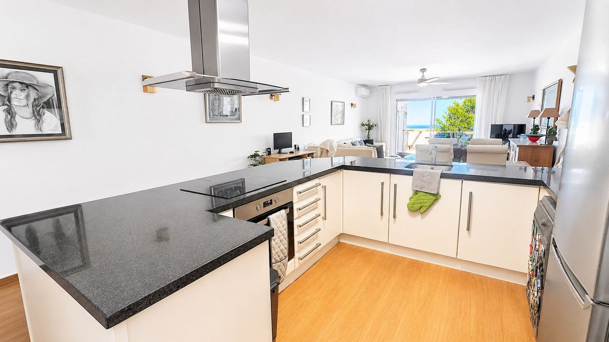 Modern kitchen with black countertops, white cabinets, and a view of the sea through large windows.