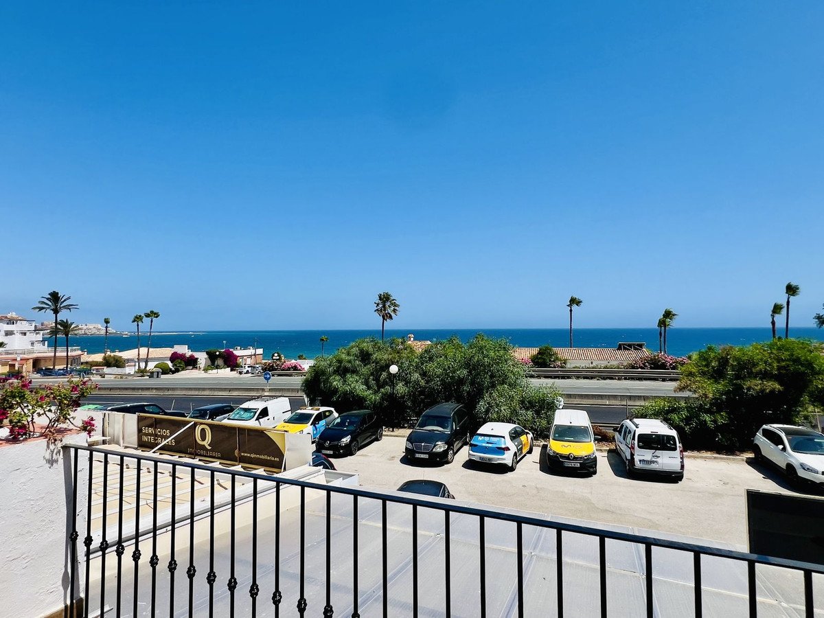 Balcony view overlooking a parking lot with the sea and palm trees in the distance