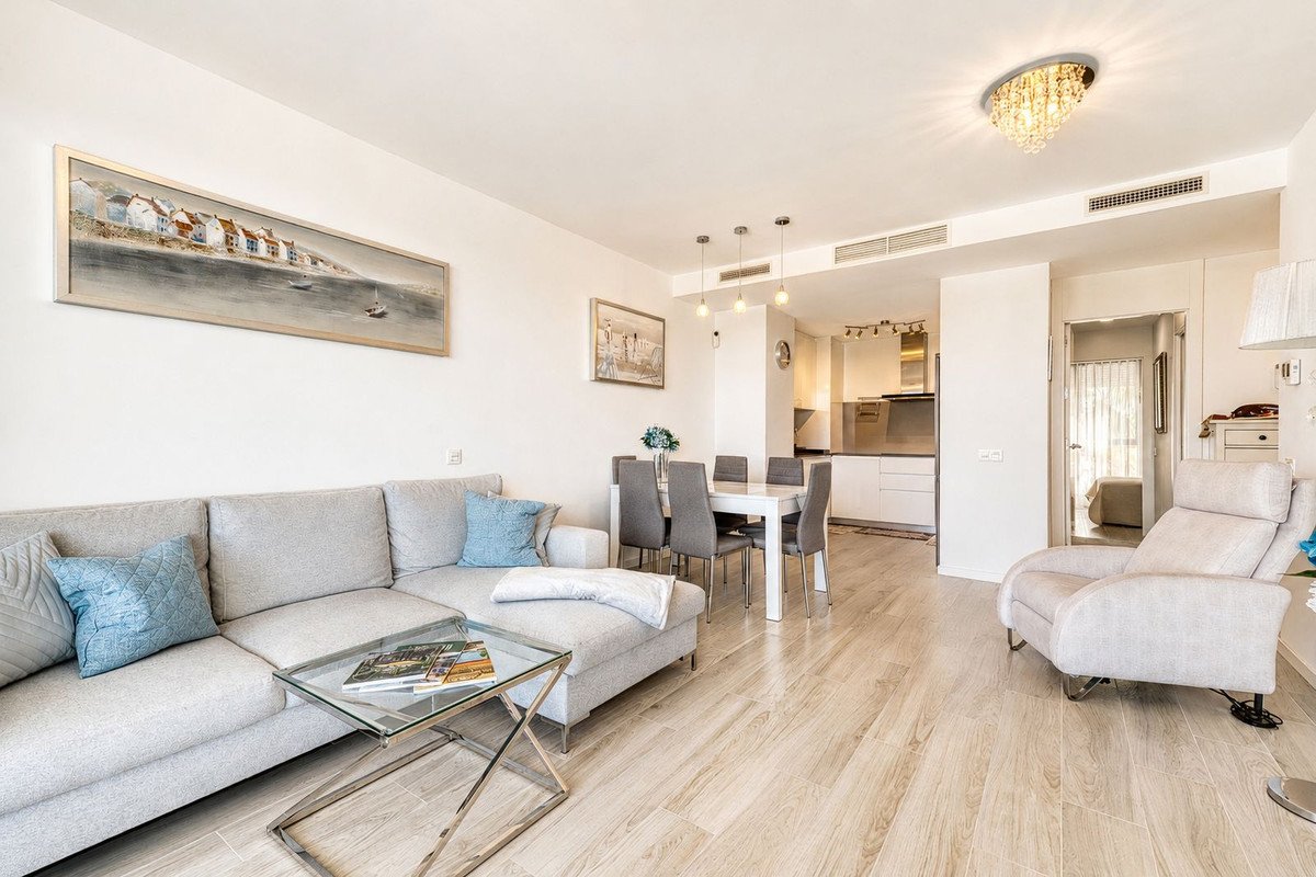 Modern living room with light gray sofa, glass coffee table, and coastal artwork on the wall
