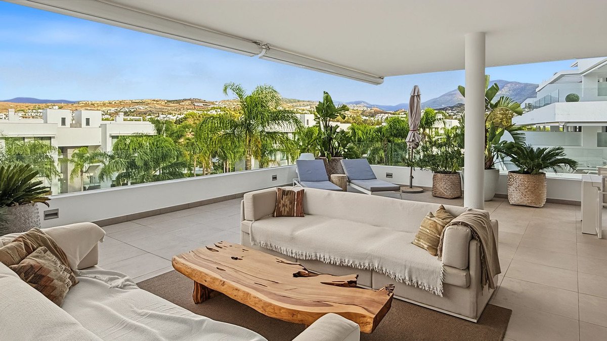 Spacious terrace with modern outdoor seating, lounge chairs, and lush greenery overlooking a scenic landscape.