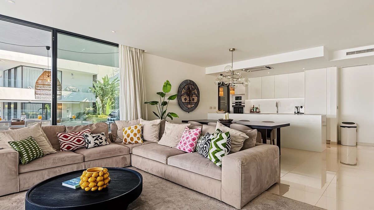 Spacious open-plan living room and modern kitchen with large sectional sofa, dining area, and large windows with outdoor views.