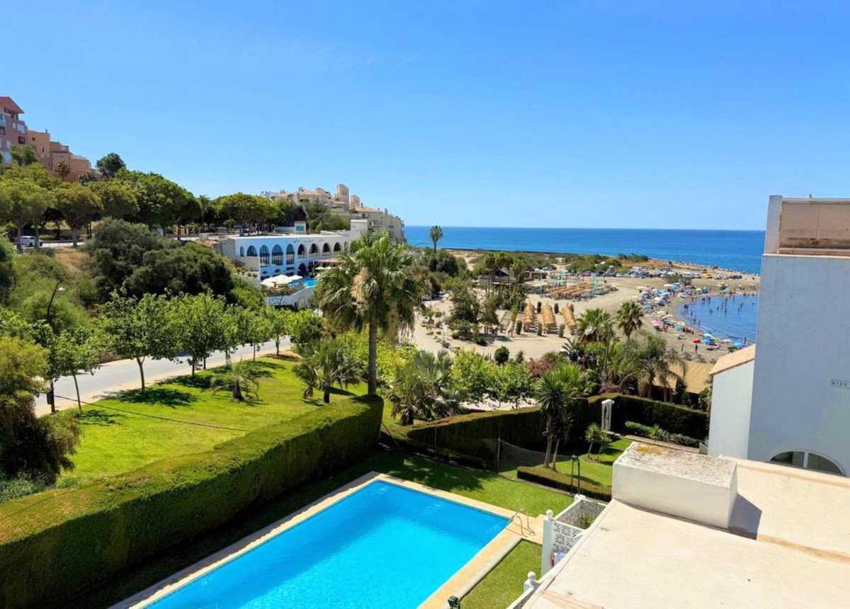 Sea view from a balcony with pool, palm trees, and beach below.