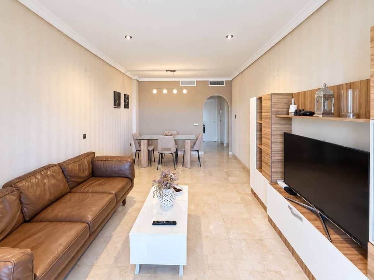 Modern living and dining area with a brown leather sofa, white coffee table, and a large television unit.