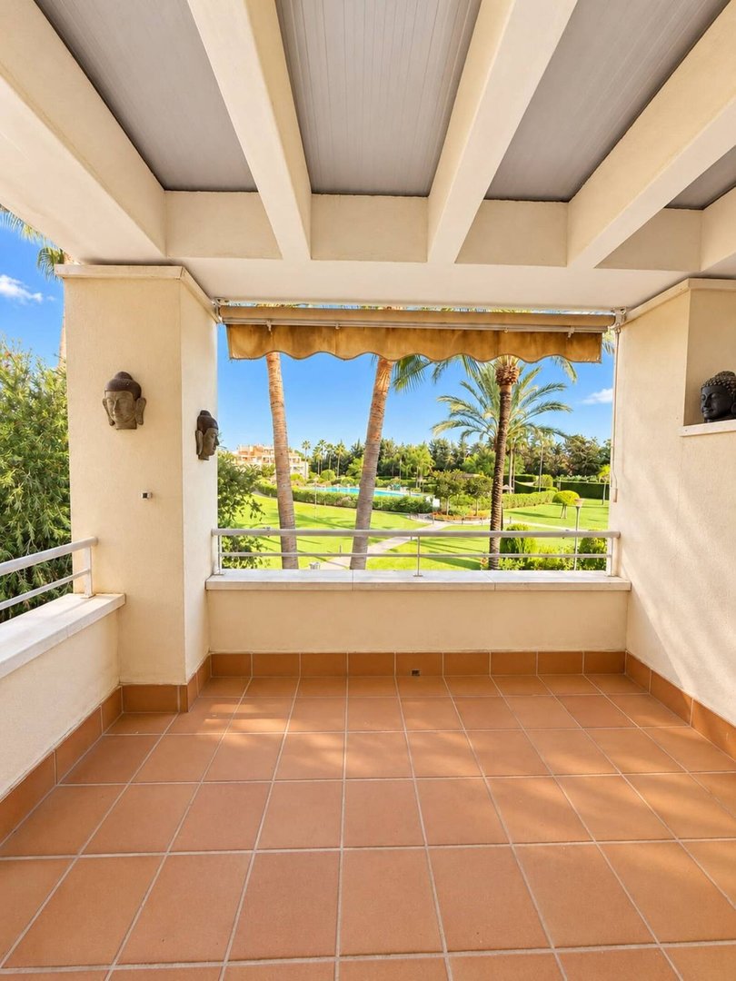 Terrace with tiled floor overlooking a lush golf course and palm trees under a bright blue sky.