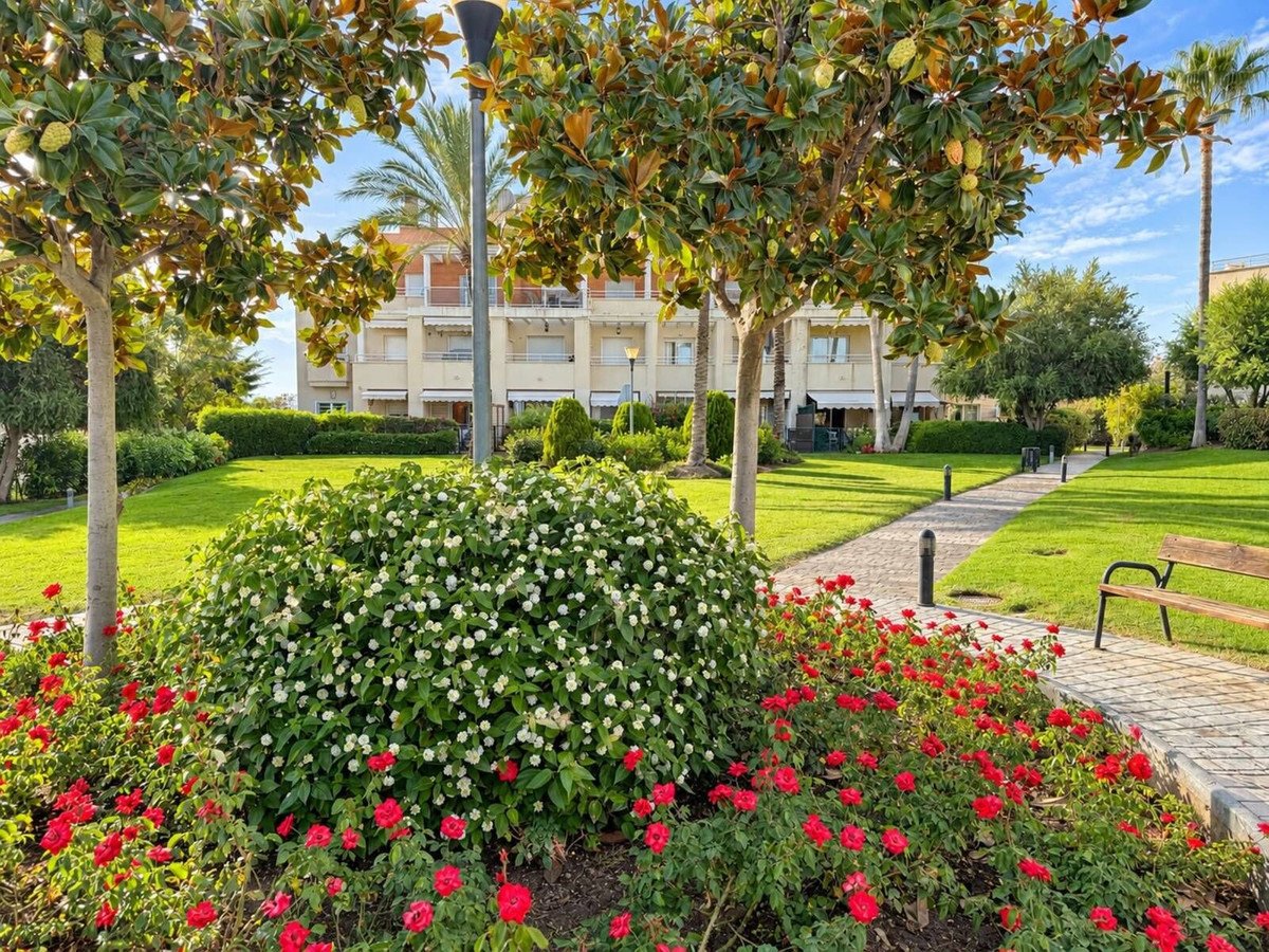 A well-maintained garden with blooming red and white flowers, trees, and a pathway leading to a building.