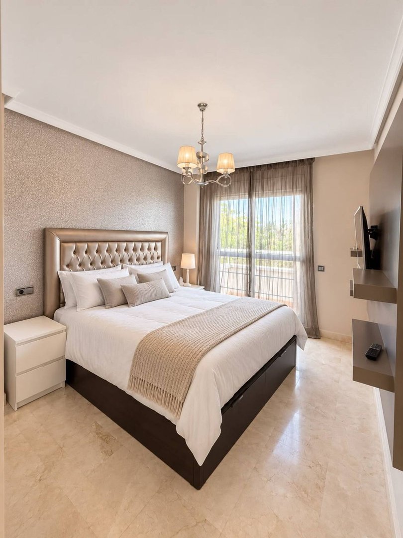 A luxurious bedroom with a queen-size bed, ornate headboard, and a view of trees from the balcony.