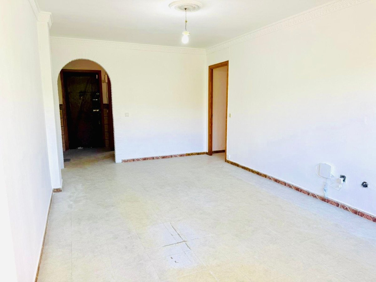 Empty room with tiled floor, white walls, arched doorway, and ceiling light fixture.