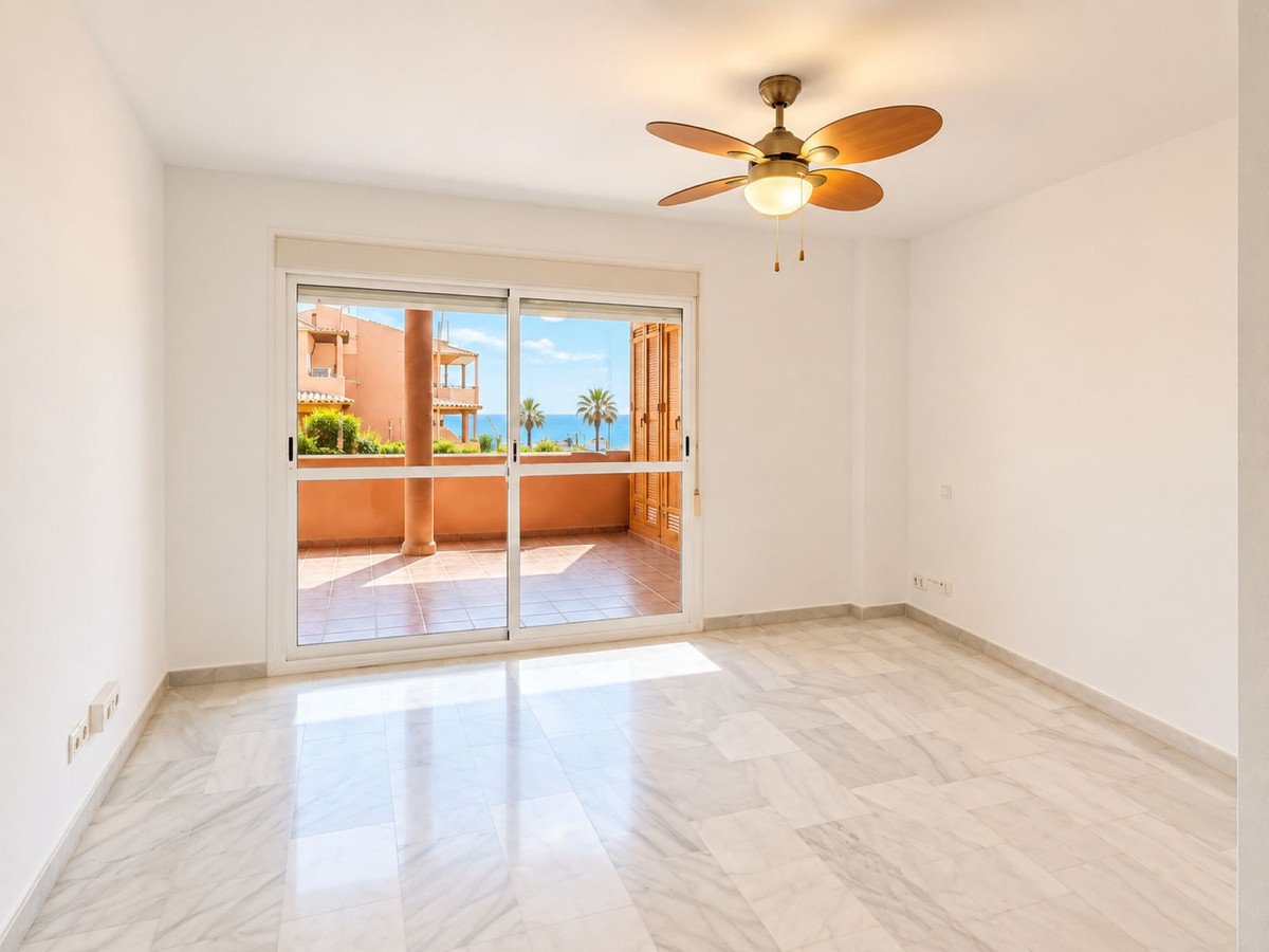 A bright bedroom with marble floors, a ceiling fan, and sliding glass doors leading to a balcony with a sea view.