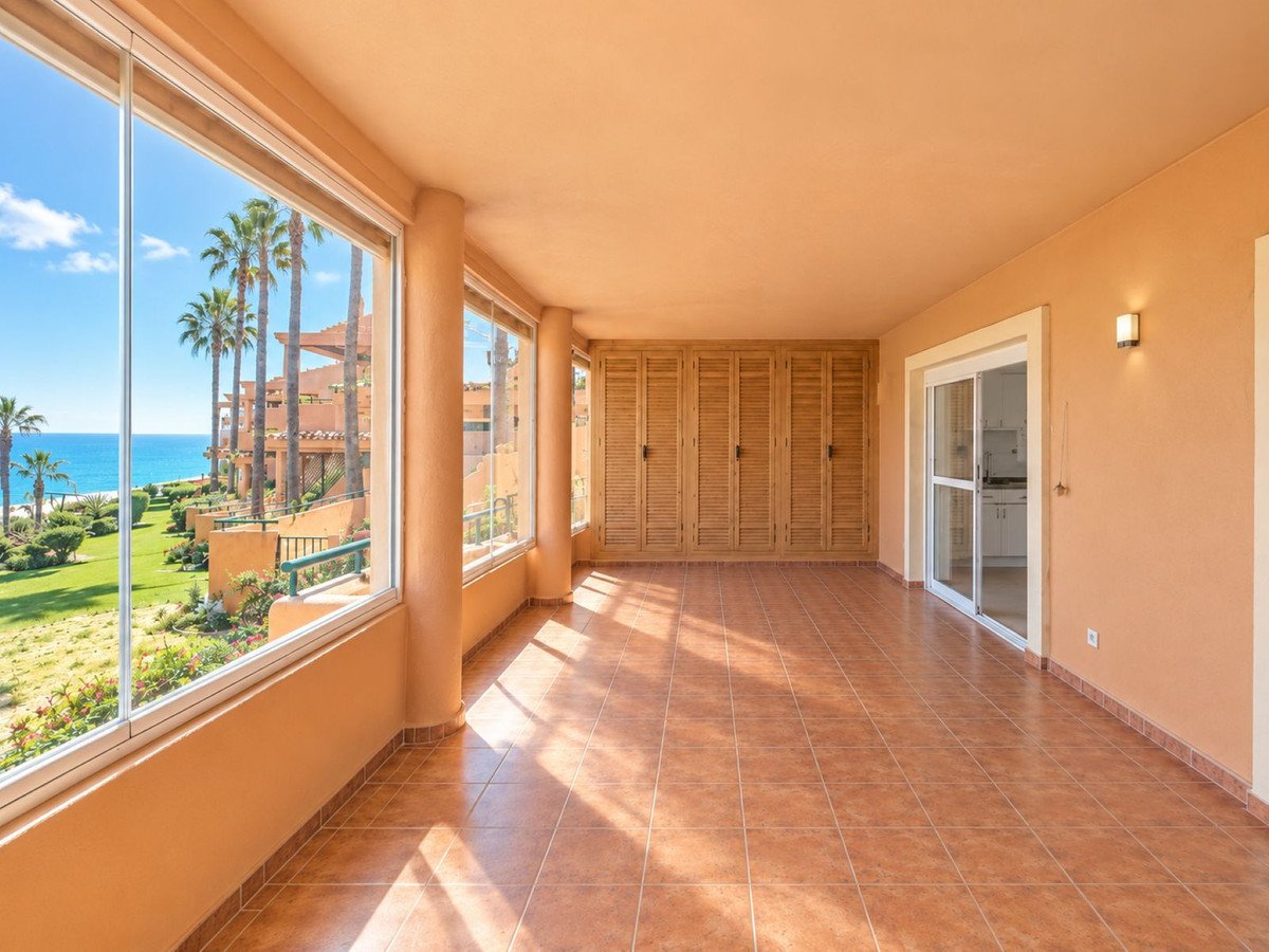 Spacious covered terrace with glass walls offering a beautiful sea view and palm trees.