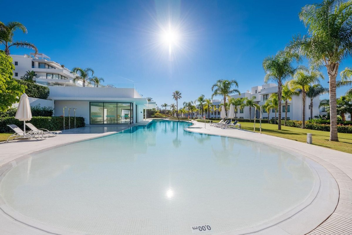 A large, modern swimming pool with resort buildings and palm trees under a bright sunny sky.