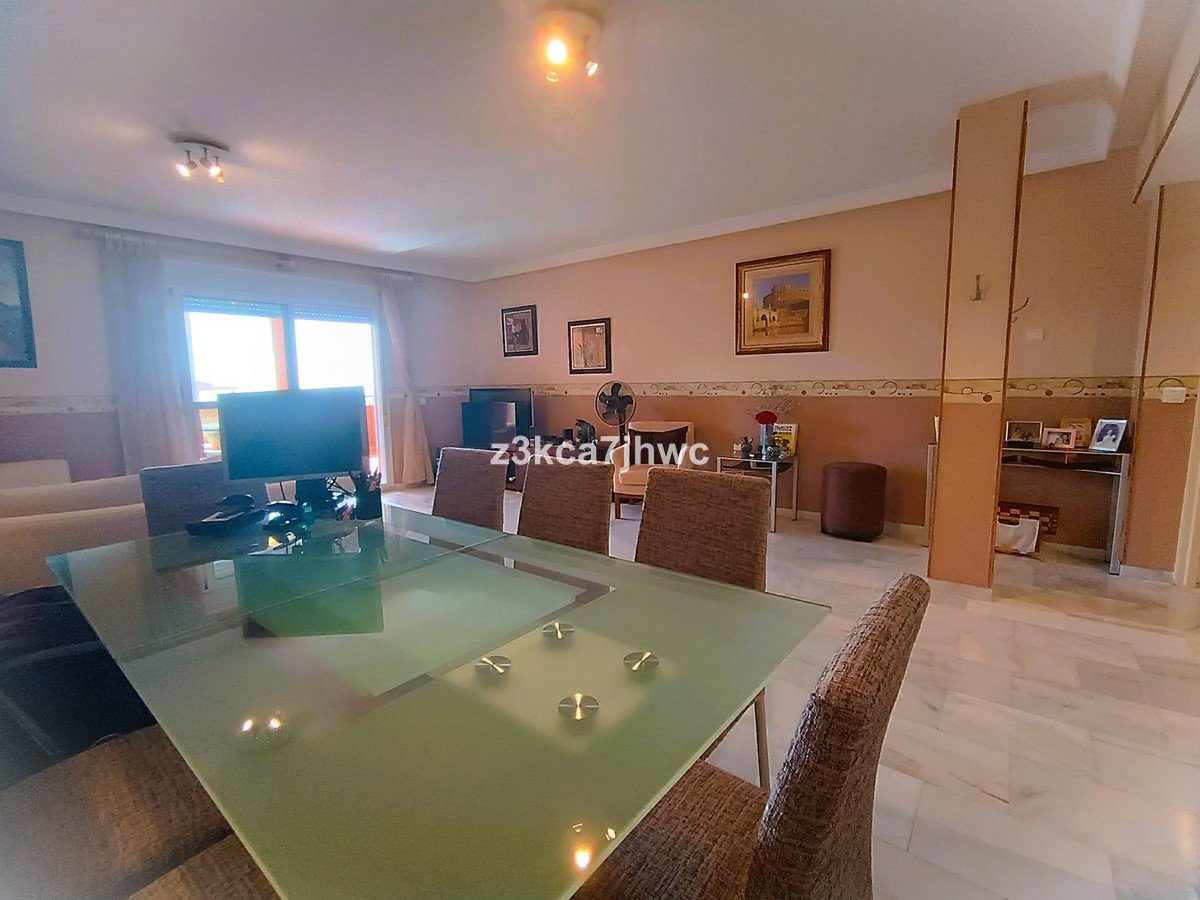 A spacious living and dining room with a glass table, comfortable chairs, and ample natural light from large windows.