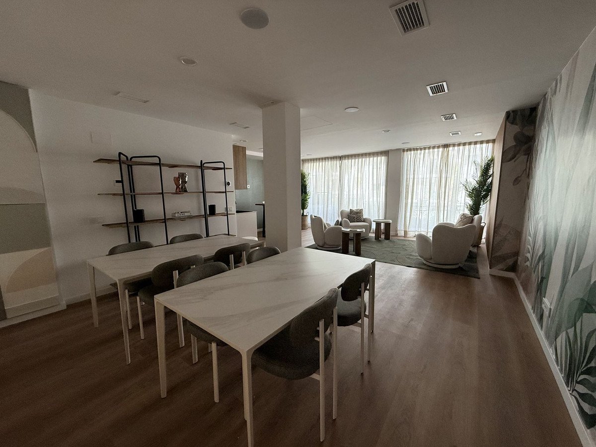 Modern dining area with two tables, chairs, and a living space with large windows and plants.